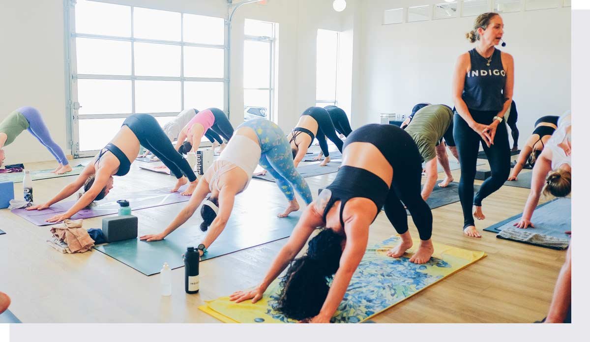 Yoga class doing downward facing dog with instructor watching
